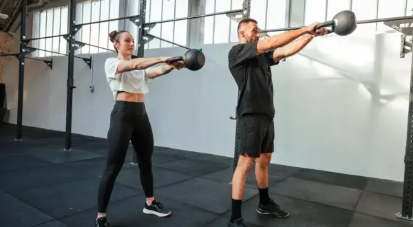 Kobieta i mężczyzna wykonują ćwiczenia z kettlebellami w siłowni.